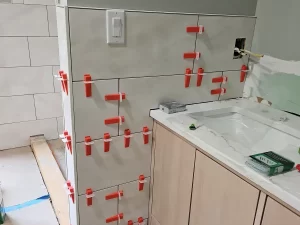 Bathroom remodel in progress with large tile installation around the vanity area, red spacers used for alignment.