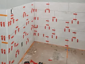Tile installation in progress on bathroom walls, with red spacers holding the tiles in place, part of a bathroom build-out.