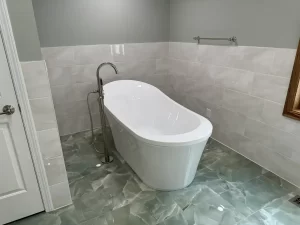 Finished bathroom remodel by Stately Kitchen and Bath with a freestanding white soaking tub, modern fixtures, and large wall tiles in a light, neutral tone.