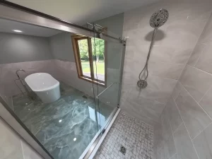 Close-up view of the shower area featuring a rainfall showerhead and frameless glass enclosure. Bathroom remodel by Stately Kitchen and Bath.