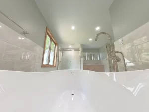POV view from the freestanding bathtub and floor-mounted faucet in a modern bathroom remodel by Stately Kitchen and Bath, with a walk-in shower and dual vanity in the background.
