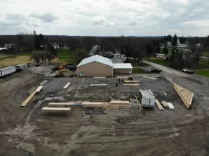 Aerial view of the Bennington Highway Department construction site showing poured concrete piers and Perma-Column brackets being set into the ground, with equipment and materials arranged on-site.