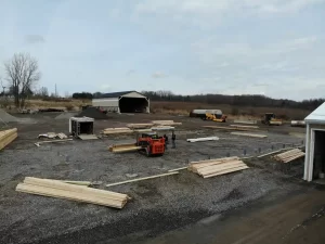 Wide shot of the construction site at the Bennington Highway Department, displaying the arranged construction materials, equipment, and workers preparing the concrete piers and Perma-Column brackets.