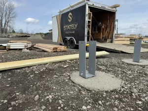 Closer view of the Bennington Highway Department pole barn construction site, showing the concrete piers and workers setting up Perma-Column brackets before the framing process.