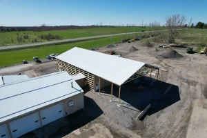 Aerial view of the Bennington Highway Department pole barn construction, showcasing the newly installed metal roof and partially constructed walls with open framing, surrounded by equipment and materials.