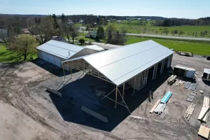 Close-up view of the side of the Bennington Highway Department pole barn during construction, showing the completed metal roof and open-framed walls, with construction vehicles and equipment on-site.