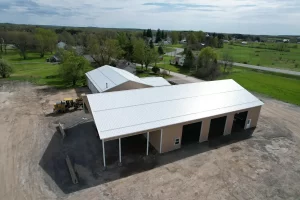 Aerial shot of the Bennington Highway Department pole barn nearing completion, featuring the installed metal roof, support columns, and open wall framing, with a grader parked nearby.