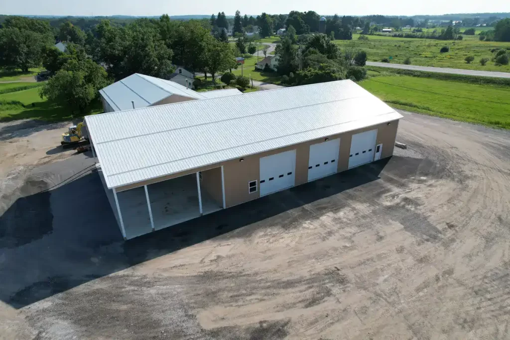 Wide shot of the completed Bennington Highway Department pole barn, showcasing the metal roof, concrete foundation, and large garage doors, with surrounding landscape visible.