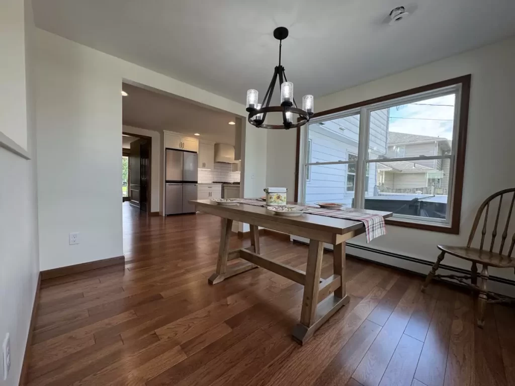 Dining area with rustic wood table, elegant chandelier, and large window overlooking the backyard for a cozy, inviting atmosphere.