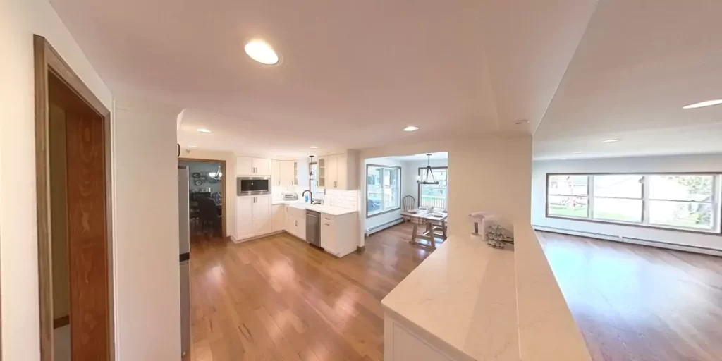 Kitchen with white cabinets, marble counters, and wood flooring, seamlessly connecting to living and dining areas for an open-concept layout.