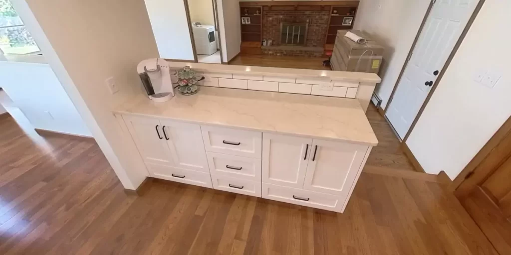 White cabinetry with marble countertop in an open kitchen setup, featuring classic black handles for a modern yet rustic look.