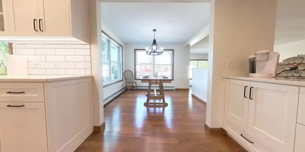 Dining room with rustic table, natural wood flooring, and bright windows in a cozy, open-concept home addition.
