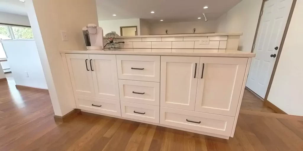 Spacious kitchen coffee bar area with ample natural light, featuring hardwood floors and white cabinets.