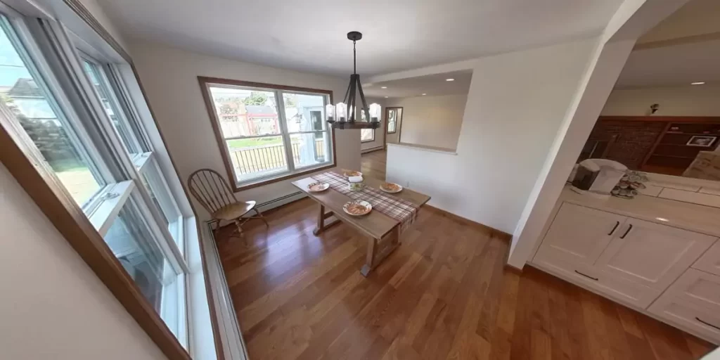 Dining room with rustic table, natural wood flooring, and bright windows in a cozy, open-concept home.