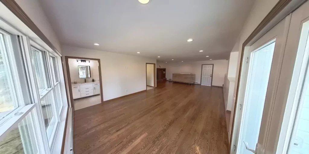 Wide view of hardwood flooring in a spacious, light-filled home with bathroom and living areas.
