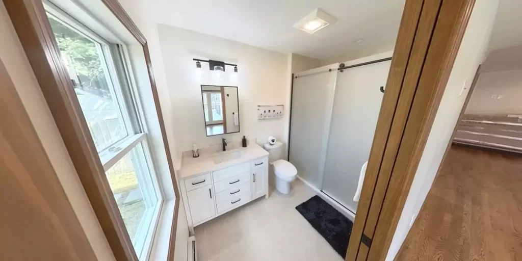 Modern bathroom with a large window, white vanity, and glass shower door for a bright, minimalist design.