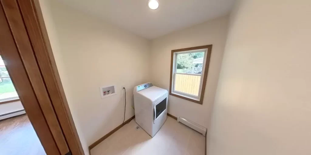 Compact laundry room with single window, white dryer, and bright natural light.