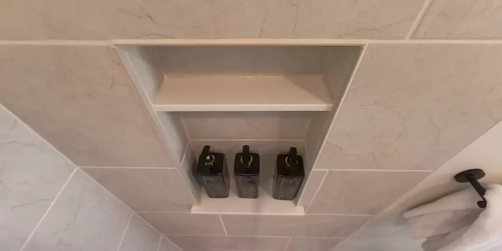 Shower niche with black bottles and dark hardware accents in a beige-tiled shower for a sleek, modern bathroom look.