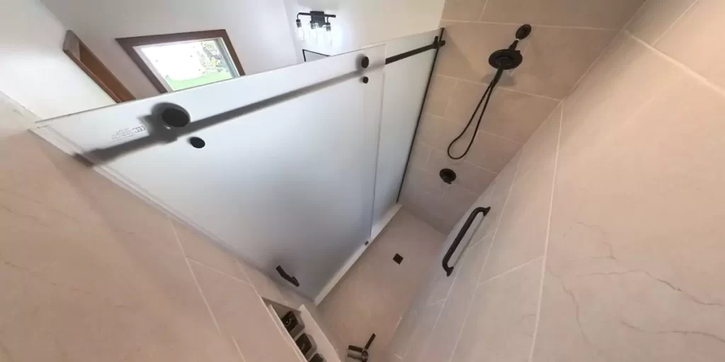 Modern shower with frosted glass, dark hardware, and beige tile in a newly renovated bathroom.