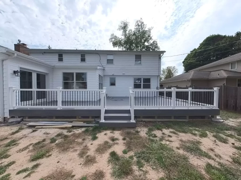 Rear view of a modern white home with a new spacious deck, featuring white railing and black accents. Ideal for outdoor entertainment.