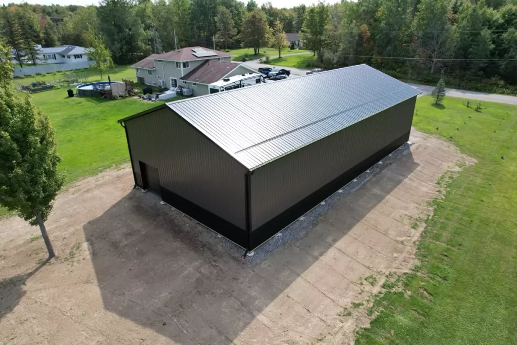 Side view of Stately’s post-frame barn, showing the long black roofline and charcoal steel siding in a residential setting.