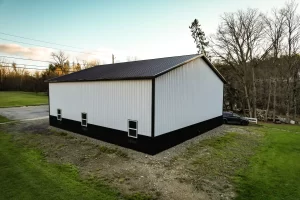 Rear corner of a Stately pole barn with black wainscot and vented eaves, emphasizing superior moisture prevention and structural quality.