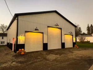 Angled view of a Stately-built pole barn at dusk, featuring illuminated gooseneck lights and custom wainscot design in Holland, NY.