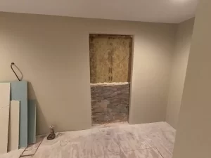 Construction progress showing finished drywall, cutout for new man door, and new subfloor.