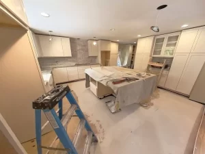 Modern kitchen renovation underway with white cabinetry, covered countertops, and subway tile backsplash.