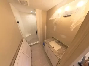 Newly tiled bathroom under renovation with glass shower, bright lighting, and contemporary vanity.