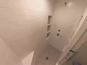 Walk-in shower installation with white subway tiles and hexagonal tile flooring.