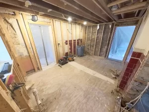 Kitchen under renovation showing bare wooden studs and old sub-flooring.