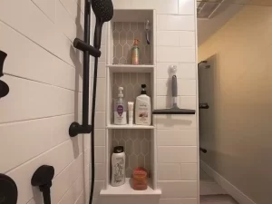 Close-up of a modern shower niche with hexagonal tiles, featuring black hardware and organized bath products.