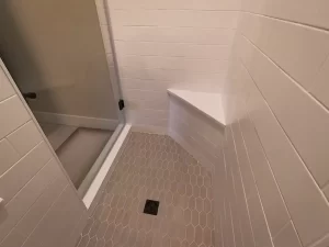 Shower corner with a built-in bench, hexagonal floor tiles, and clean white subway tiles.