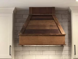 Rustic reclaimed wood range hood over a sleek tiled backsplash, a signature design by Stately Kitchen and Bath.