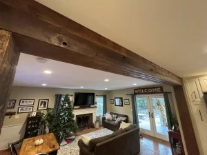 Rustic reclaimed wood beam decorates an open-concept living room with a welcoming farmhouse design, highlighting warm tones and cozy aesthetics.