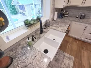 Elegant granite countertop and double farmhouse sink with black fixtures designed by Stately Kitchen and Bath in Clarence, NY.