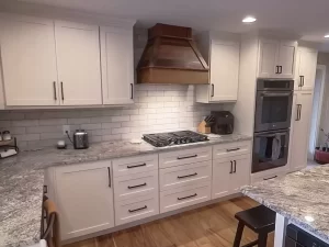 White kitchen cabinets with rustic reclaimed wood vent hood and modern oven in a custom Stately Kitchen and Bath remodel.