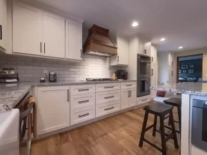 Custom kitchen remodel by Stately Kitchen and Bath featuring white cabinets, granite countertops, and a wooden range hood.