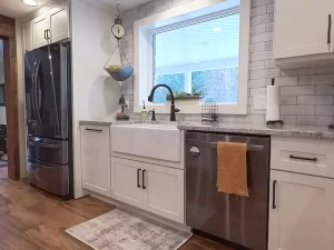 Granite countertop kitchen sink with a farmhouse-style design, remodeled by Stately Kitchen and Bath, overlooking a serene backyard view.