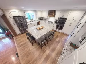 Top-down view of a modern kitchen with a large granite island, stainless steel appliances, and hardwood flooring by Stately Kitchen and Bath.