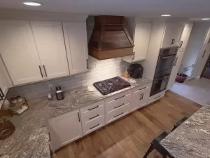 Overhead view of a custom-designed kitchen featuring granite countertops, a rustic wood range hood, and sleek white cabinetry by Stately Kitchen and Bath.