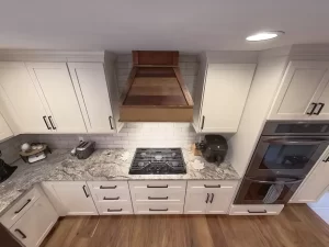 Close-up of a modern kitchen layout with a wooden range hood, dual ovens, and premium granite counters by Stately Kitchen and Bath.