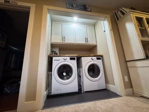 Compact laundry area with front-loading washer and dryer, white cabinetry, and a custom wood countertop.