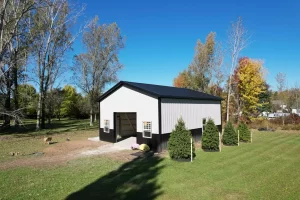 Side view of Stately Pole Barn with black wainscot, surrounded by greenery and trees.
