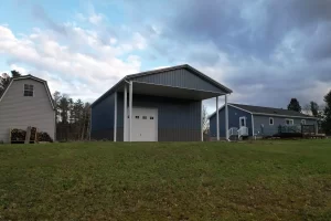 Ground-level shot of pole barn rear porch with white post wrap, showcasing covered entry and blue siding.