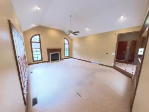 Spacious Amherst NY living room pre-remodel with vaulted ceilings, beige carpet, and natural wood trim around fireplace and windows.