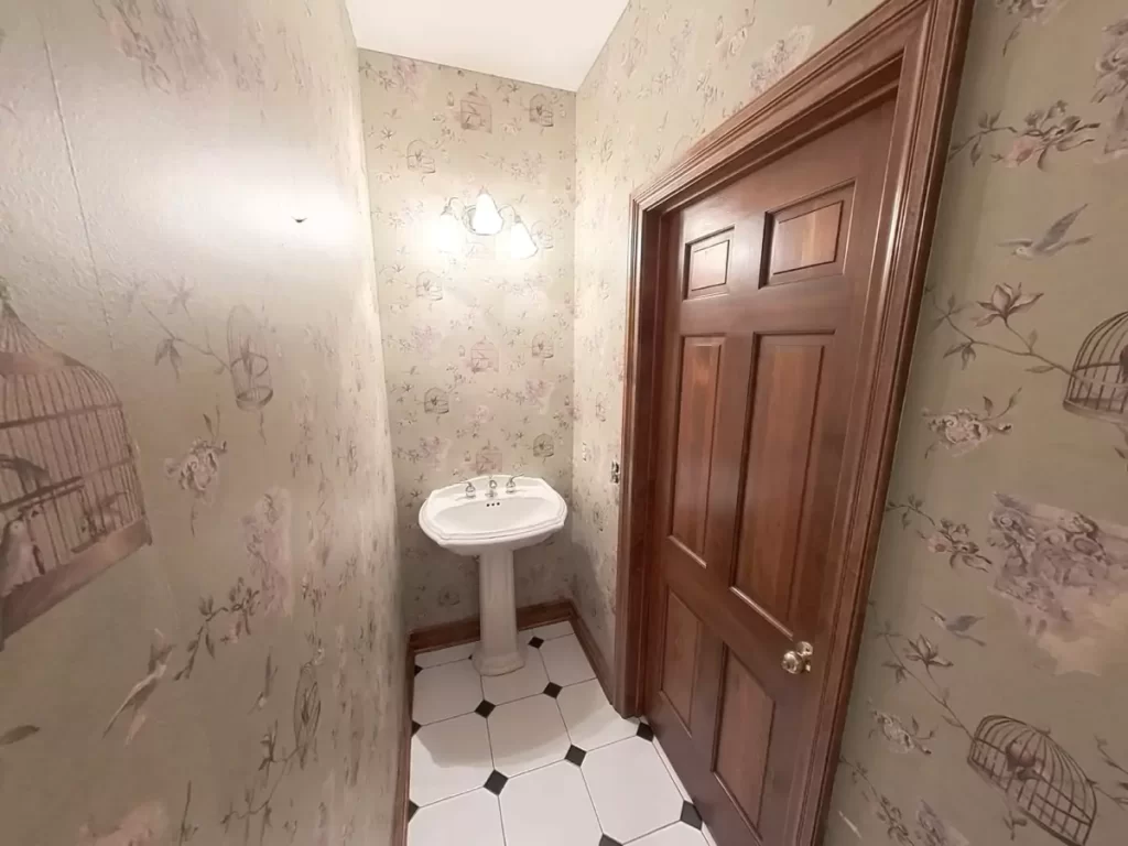 Vintage Amherst NY powder room with floral birdcage wallpaper, pedestal sink, and black and white tile flooring.