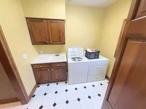 Traditional Amherst NY laundry room with tile flooring, wood cabinets, utility sink, and top-load washer and dryer.