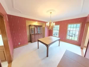 Amherst NY dining room pre-remodel with red patterned wallpaper, large windows, brass chandelier, and vintage hutch.